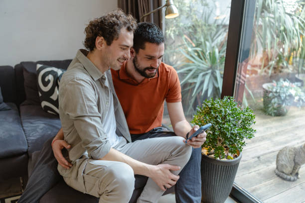 istock Gay couple using a smartphone while sitting in a comfortable modern living space 2196839278