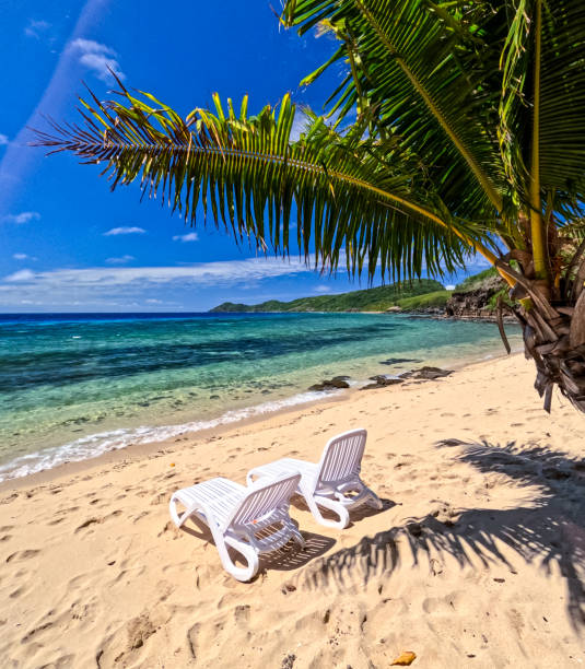 istock On a tropical island beach, white deck chairs are set up for sunbathing, with a blue channel and distant coral as the backdrop 2196840674
