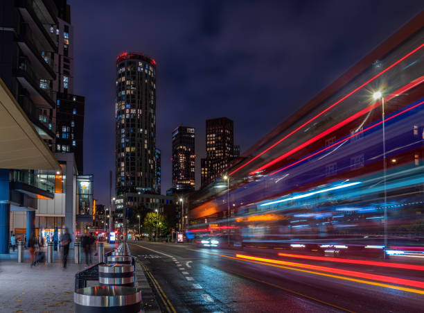 London, United Kingdom - October 27, 2024: A vibrant city scene of London at night featuring tall illuminated buildings . A bus is captured in motion, creating streaks of light, blurred pedestrians.