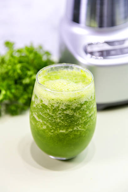 A refreshing glass of green juice prepared in a blender, featuring vibrant green parsley in the background. Perfect for a healthy lifestyle, this natural juice is packed with vitamins and flavor.\