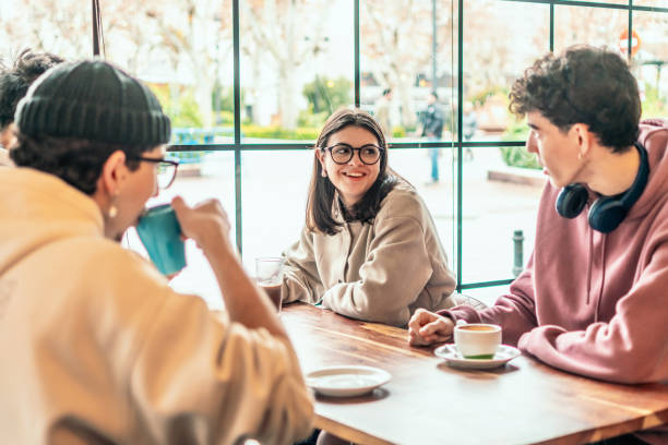 istock Young professionals relaxing, drinking coffee, chatting animatedly while sitting near sunlit cafe window, enjoying warm, friendly atmosphere 2196871756