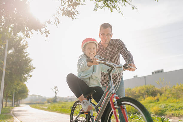 istock Father teaching daughter riding bicycle in park during sunny day 2196880485