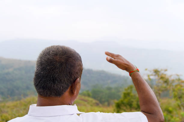 An Asian man with short black hair stands with his back to the camera, looking out at a majestic mountain