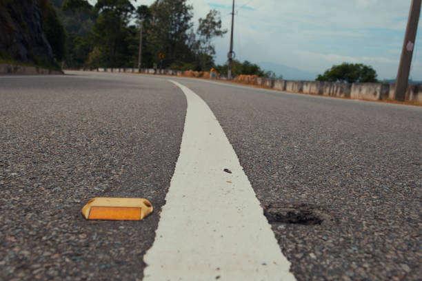 A close-up view of a curved road with a white line and a yellow reflective marker embedded in the asphalt near the white line