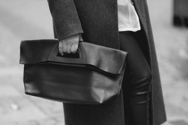 A woman in a black raincoat with a black leather bag.