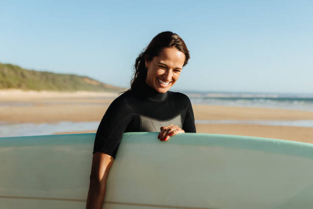 istock Smiling woman surfer standing on a sandy beach with her surfboard under sunlight 2196894774