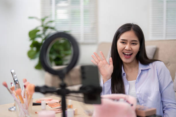 istock Beauty broker waving at the camera during a live broadcast, engaging with viewers while showcasing makeup products. 2196895598