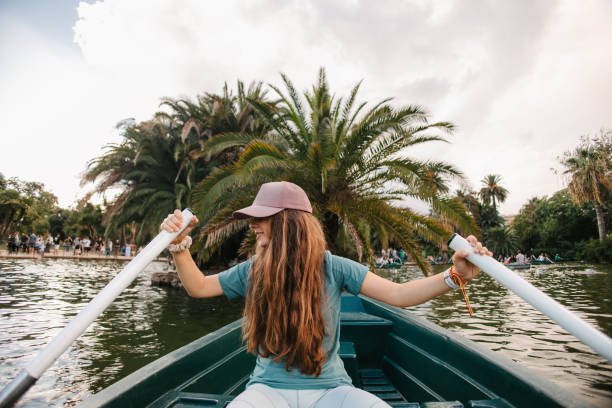 Smiling mature woman with friend rowing boat in lake. Active females are enjoying boating in forest during vacation. They are wearing casuals.