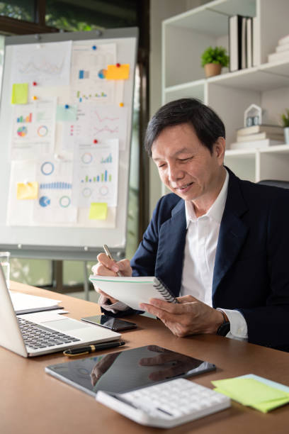 istock Elderly Asian businessman smiling while taking notes in a notebook during a meeting at a modern office. 2196896561