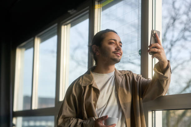 istock Young man taking a selfie while enjoying a cup of coffee by the window 2196898220
