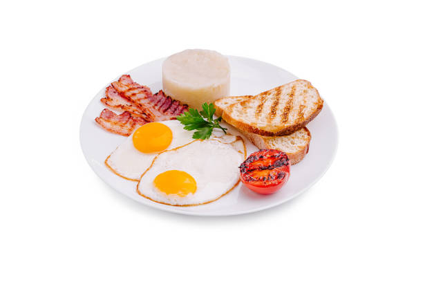 A delicious breakfast featuring two fried eggs with sunny-side up yolks, crispy bacon strips, grilled tomato, and toasted bread arranged neatly on a white plate.