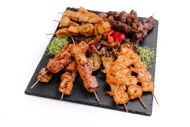 Grilled skewers featuring shrimp, beef, and chicken served on a slate platter with vegetables