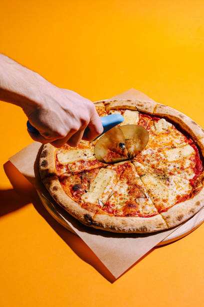 Delicious pizza being cut with a circular cutter on a vibrant yellow background
