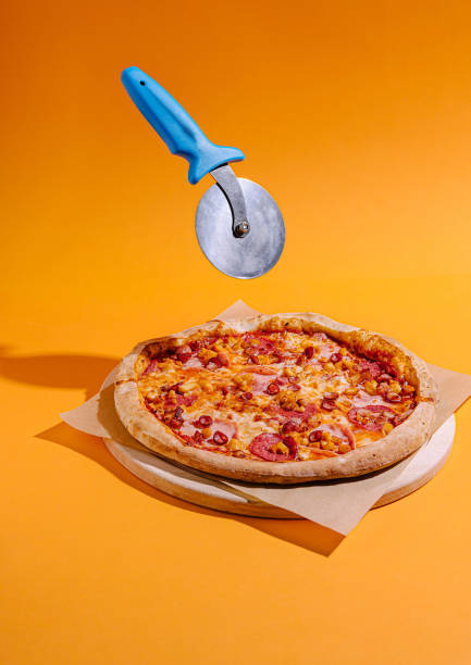 istock Pizza with vibrant orange background and a pizza cutter floating above ready for slicing 2196907413