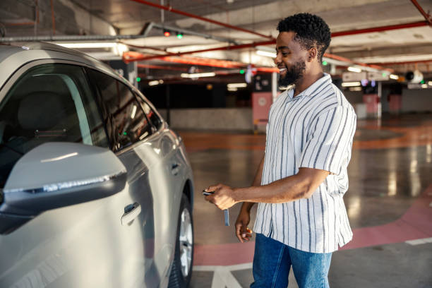 Cheerful young multicultural car driver is locking car door on vehicle in public garage.