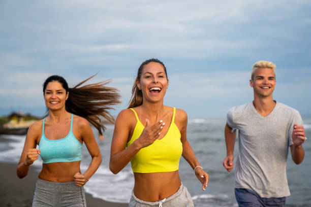 Group running on beach jogging having fun training. Exercising runners training outdoors living healthy active lifestyle. Multiracial fitness runner people working out together outside