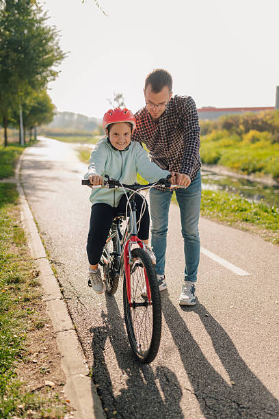 istock Father teaching daughter riding bicycle in park during sunny day 2196918165