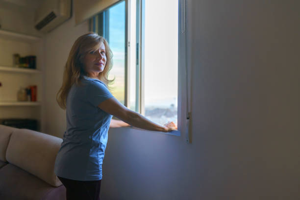istock Thoughtful woman looking out open window at sunset from home 2196919128