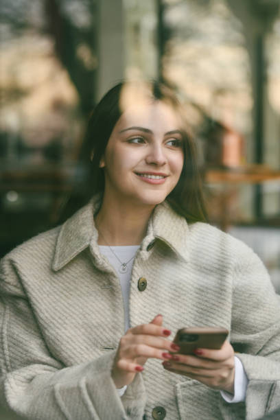 istock Joyful Female Admiring Views From Coffee Shop's Window While Holding Telephone 2196924251