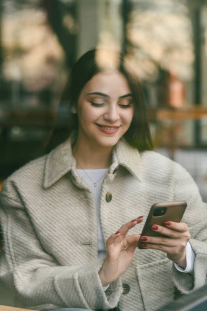 istock Beautiful Female Smiling While Texting With Crush Sitting in Restaurant Next to Window 2196925240