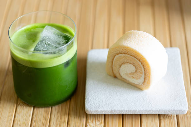 iced matcha drink with roll cake on wooden table background. Green tea drink with ice. Iced matcha in a glass with sweet. Closeup.