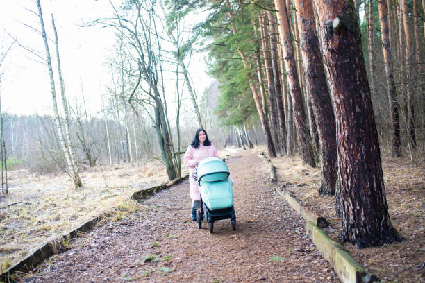 istock mother walks with a sleeping child in a green stroller in the park in cold spring 2196931207