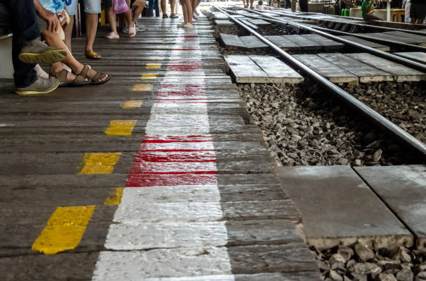 Railway tracks bordered by weathered wood and vibrant safety lines, symbolizing transportation and caution against the backdrop of a busy, crowded scene.