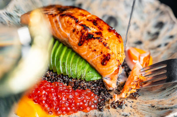 A beautifully plated dish featuring grilled salmon atop a bed of quinoa, garnished with fresh avocado slices and bright red caviar. Elegant presentation ideal for a gourmet restaurant.