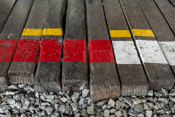 Railway tracks bordered by weathered wood and vibrant safety lines, symbolizing transportation and caution against the backdrop of a busy, crowded scene.