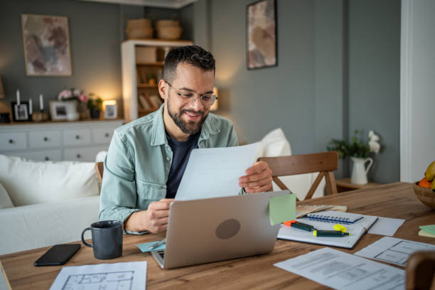 istock Man working from home, laptop and papers scattered around 2196935483