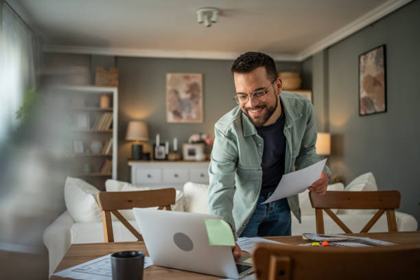istock Bearded man holding paperwork while working on a laptop in his home office 2196936260