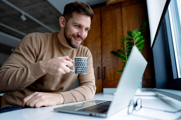 istock Young man drinking coffee and working from home on laptop 2196937143