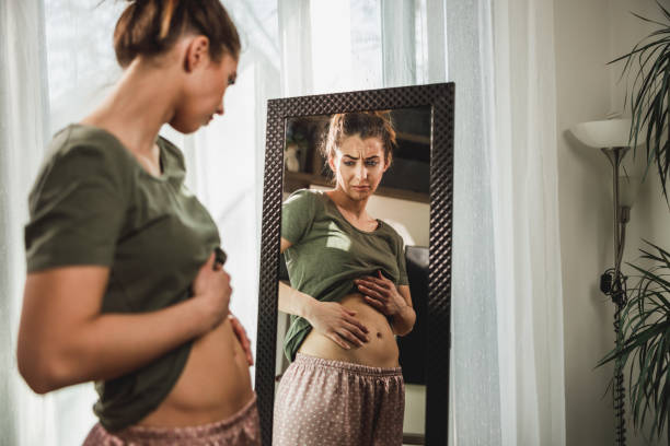 istock Woman Touching Fat Belly While Standing Near Mirror 2196939421