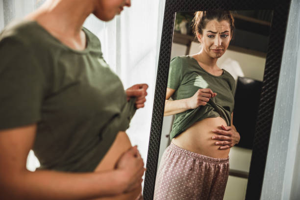 istock Woman Touching Her Belly While Standing Near Mirror 2196939484