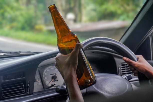 Image of driver holds beer while steering, reckless road behavior, impaired judgment, alcohol risk behind the wheel stock photo