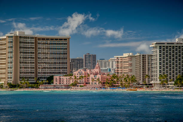 Honolulu, Hawaii, March 6, 2006: Waikiki Beach stretches out in golden splendour, its turquoise waters shimmering under the Hawaiian sun.  Framing this paradise, the iconic Royal Hawaiian Hotel, with its distinctive pink facade and Spanish-Moorish architecture, stands majestically against a backdrop of swaying palm trees.  The hotel's timeless elegance adds a touch of history and grandeur to the breathtaking coastal scene.
