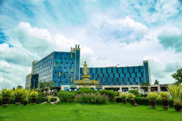 A modern commercial complex in Kigali, Rwanda, featuring striking blue architecture and a well-maintained public space. In the foreground, a statue atop a fountain adds a cultural and historical element to the vibrant cityscape. This image reflects Kigali’s rapid urbanization and economic growth, highlighting its blend of contemporary infrastructure and green spaces.