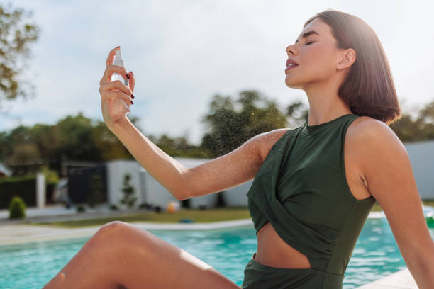 istock Woman spraying refreshing mist on her body by the pool 2196954298