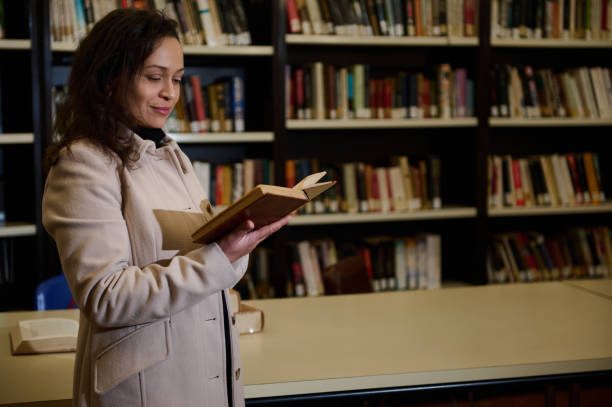istock Woman reading a book in a library surrounded by bookshelves 2196955131