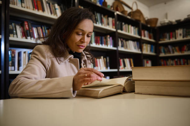 istock Woman reading a book in a library surrounded by bookshelves and texts 2196955143