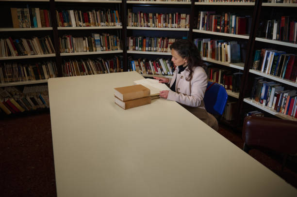 istock Woman reading documents at a library table surrounded by bookshelves 2196955227