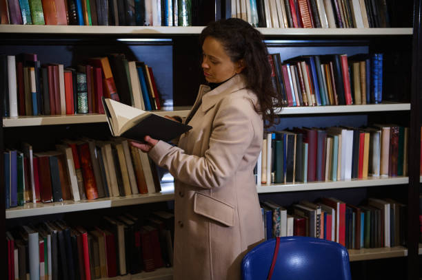 istock Woman reading a book in a library surrounded by bookshelves 2196955229