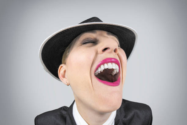 A fisheye image of a 52 year old woman with her hair pulled back and a hat on laughing out loud.