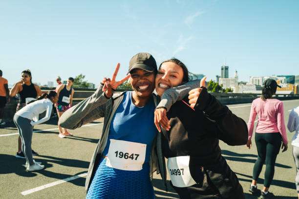 Two enthusiastic female friends are seen smiling and posing happily before participating in a half marathon. The atmosphere is lively and energetic, capturing the excitement of a race day.