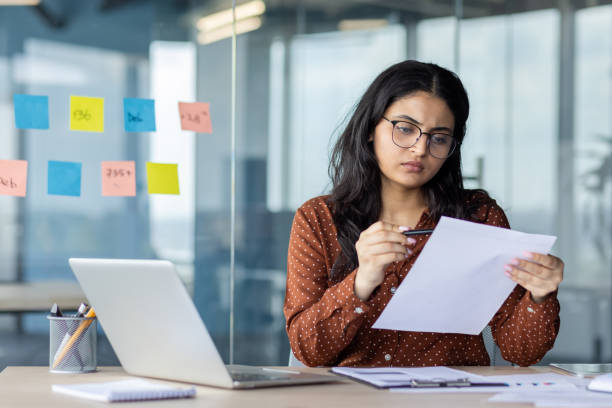 istock Serious focused woman behind paperwork reviewing analyzing and checking financial reports, financier accountant thinking and seriously concentrated at workplace inside office using laptop 2196963451