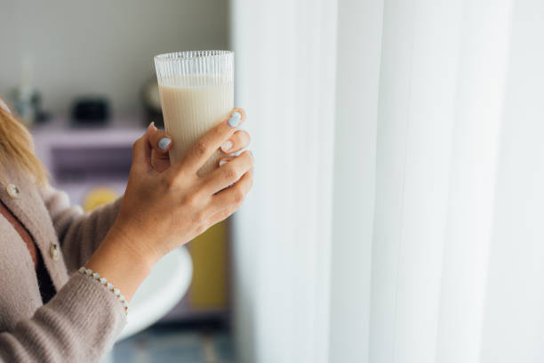 A woman is holding a glass of milk, which provides calcium and energy to the body, while relaxing in the living room at home.