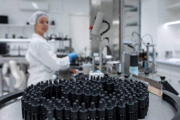 Brown medicine bottles at the beginning of the assembly line in pharmaceutical production. In the background, a worker controls the operation of the belt and closes the bottles with caps. Selective fokus.