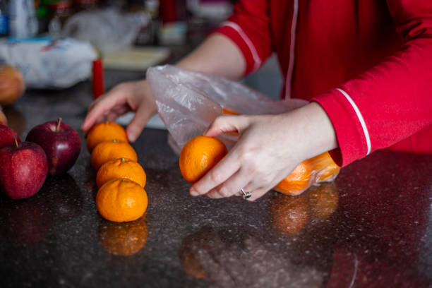 istock Woman in red jacket packing tangerines in plastic bag on kitchen counter 2196967839