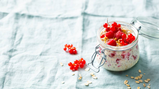 istock Overnight oats with fresh raspberries and red currants in glass jars. Blue textile background. Copy space. 2196969669