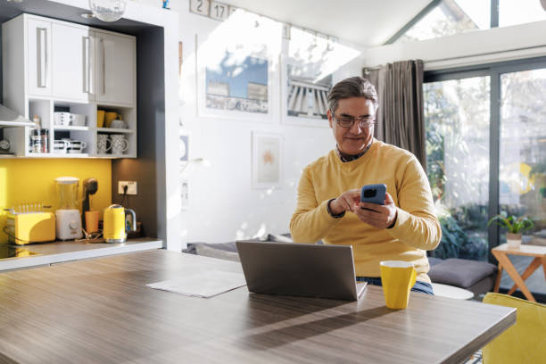 istock Mature man using phone and a laptop at home 2196969955
